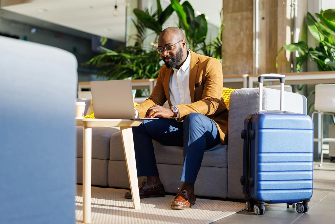 Business traveller working on a laptop beside a suitcase in an airport lounge.